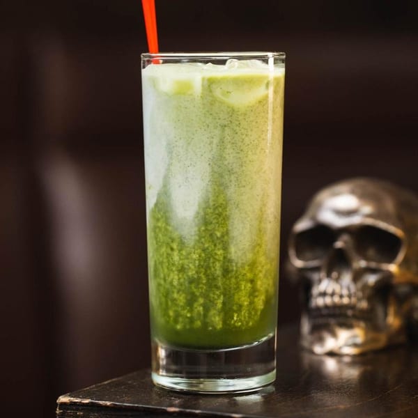 Green layered drink with ice and a red straw, next to a metallic skull.