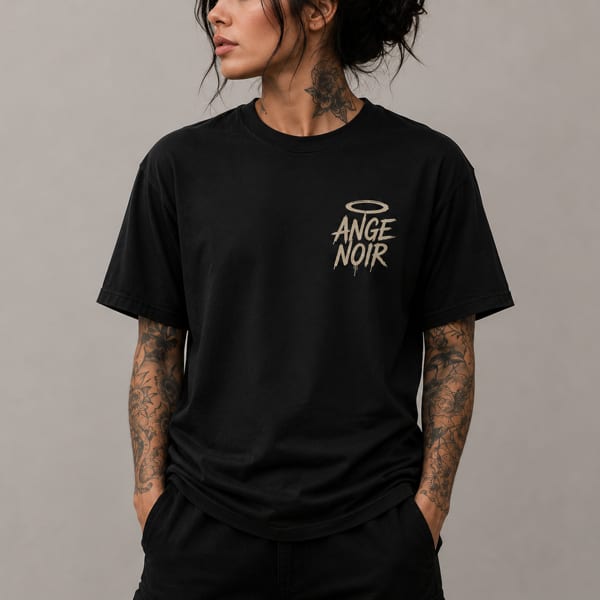 Person with neck and arm tattoos wearing a black t-shirt with "ANGE NOIR" and a halo graphic.