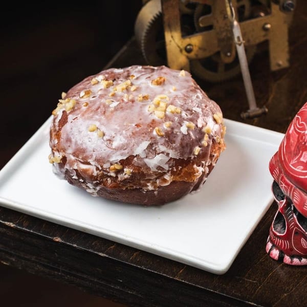A glazed donut with nuts on a white plate next to a red skull decoration.